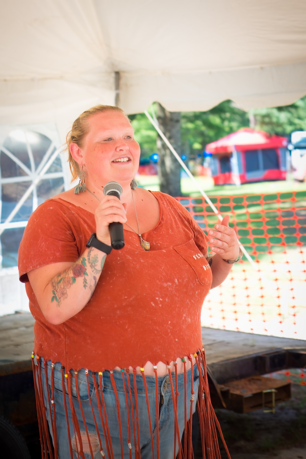 woman in orange shirt holds microphone and gives a speech
