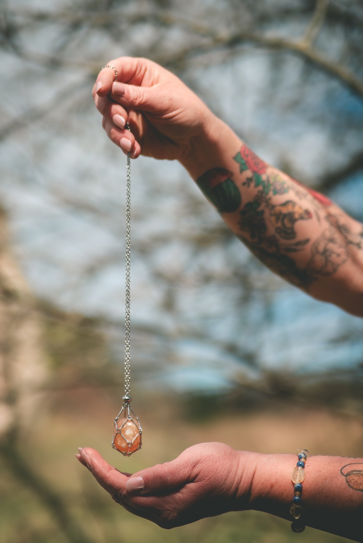 tattooed arm holds crystal necklace in the air