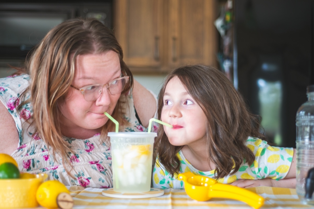 mom and daughter sip from a cup of lemonade together
