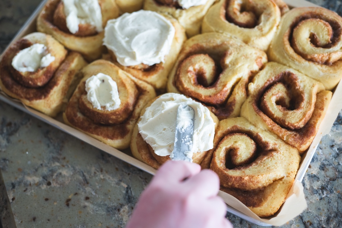 womans hand frosting home made cinnamon rolls