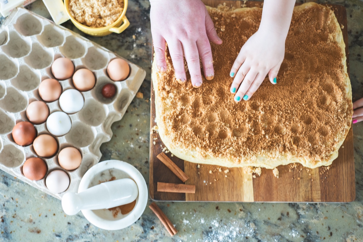 hands patting cinnamon into cinnamon rolls