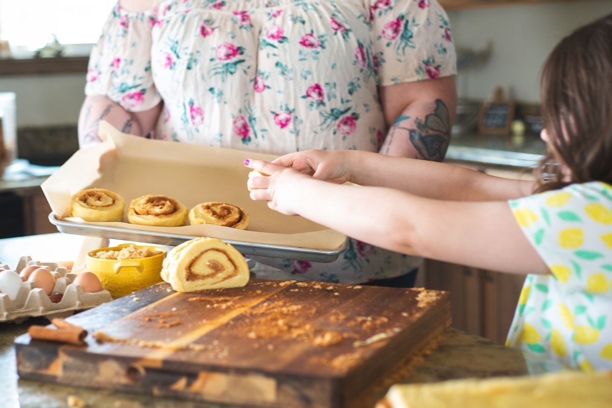 daughters hands lift cinnamon rolls onto tray