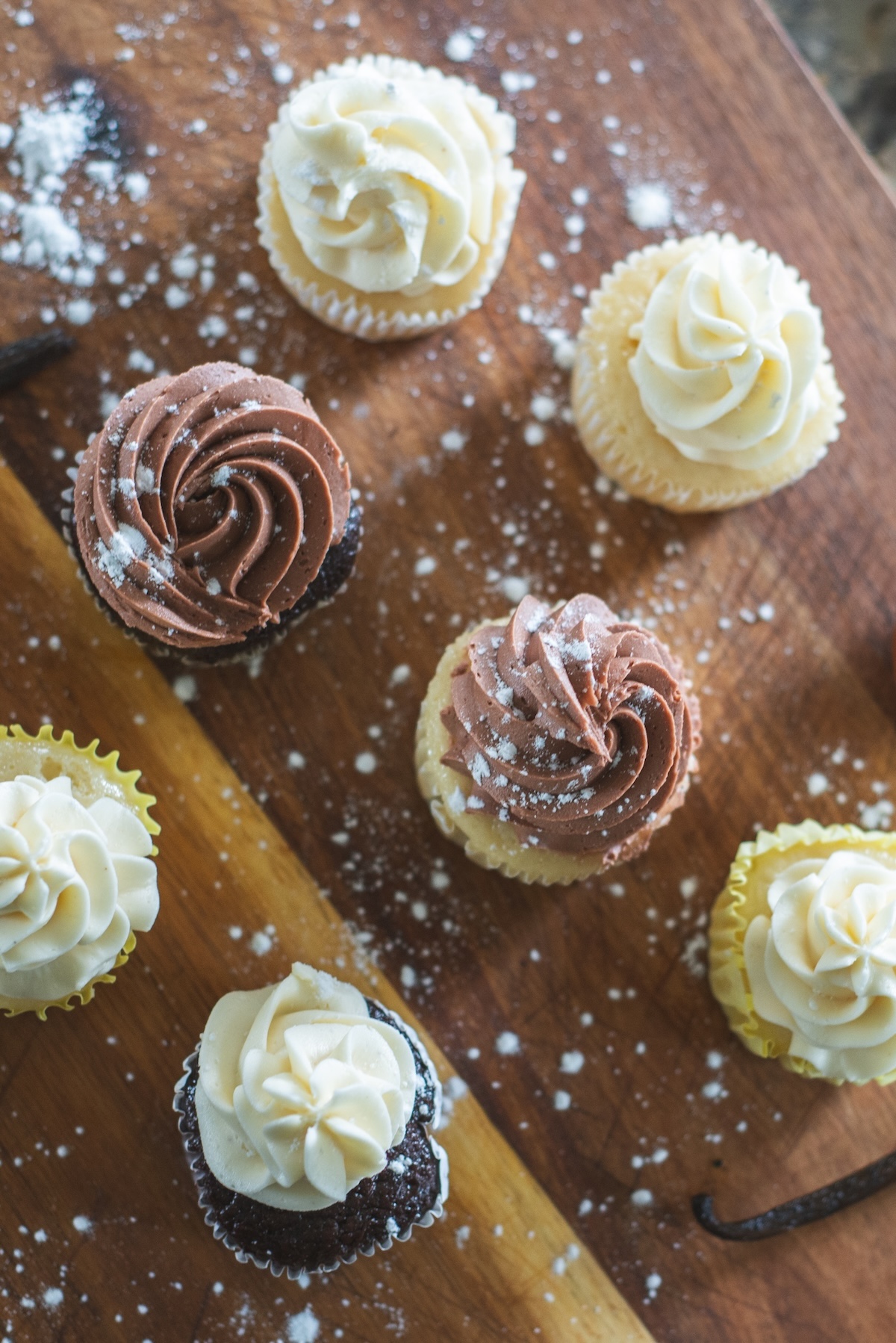 flat lay of chocolate and vanilla cupcakes with powdered sugar sprinkled around