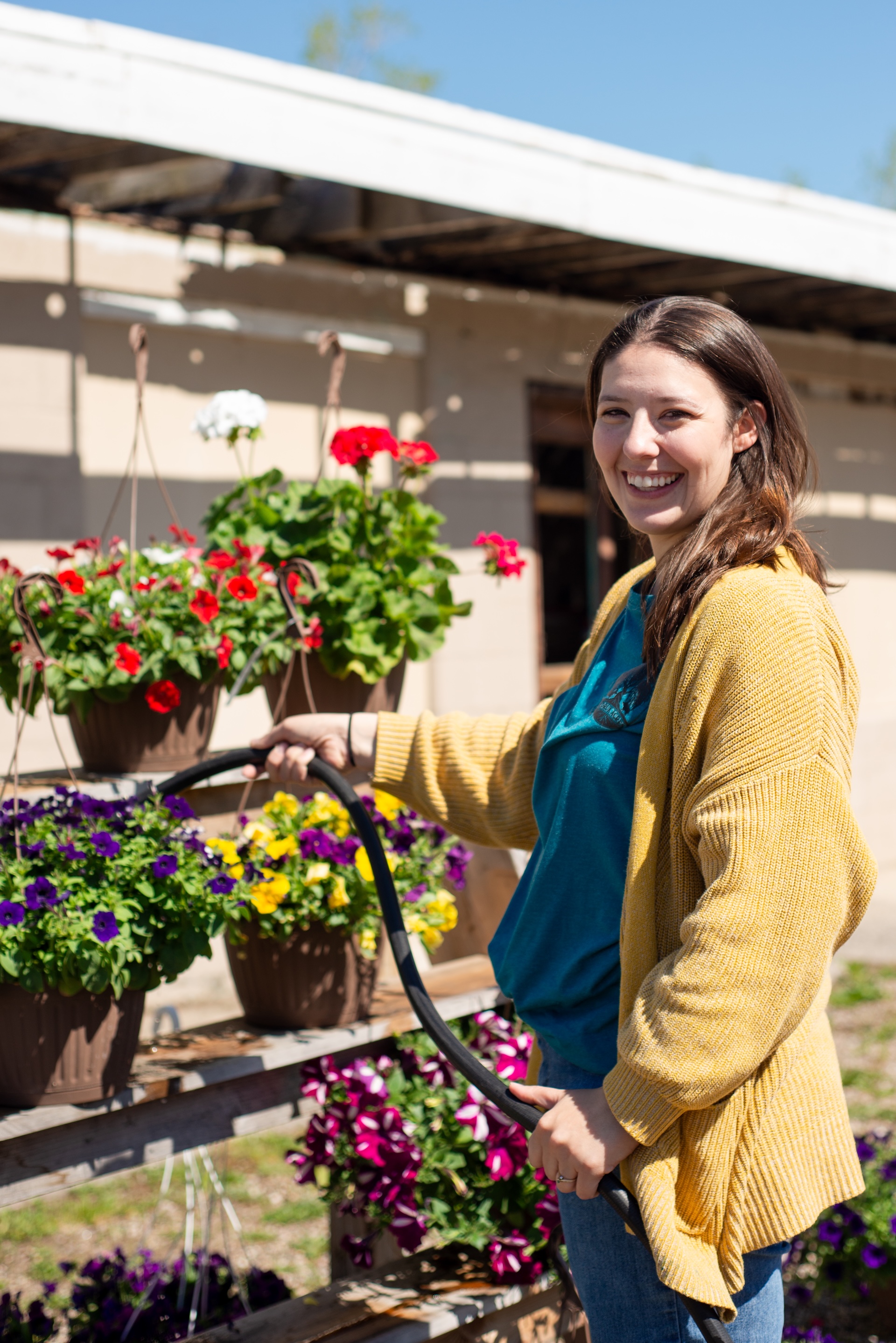 Alison of Andruk Acres watering fresh hanging flower baskets at their Manistique spring market sale