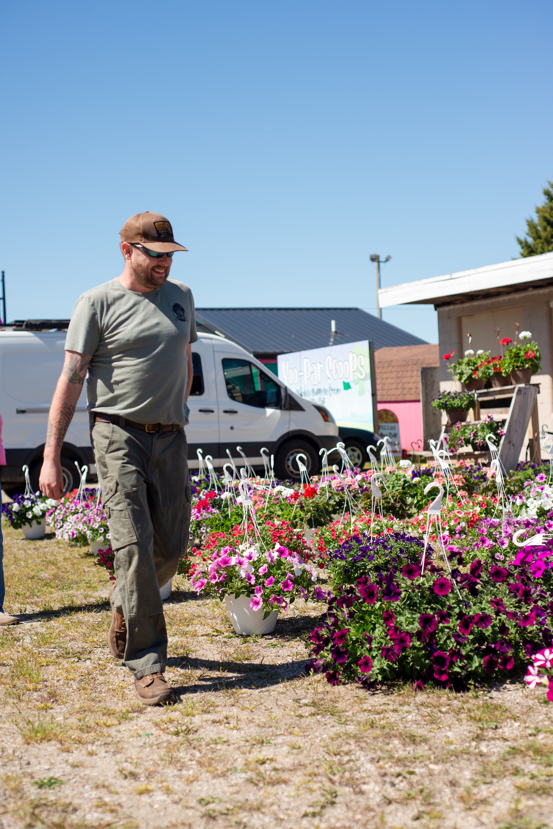 Man walks by hanging flower baskets at Andruk Acres Flower Market Event