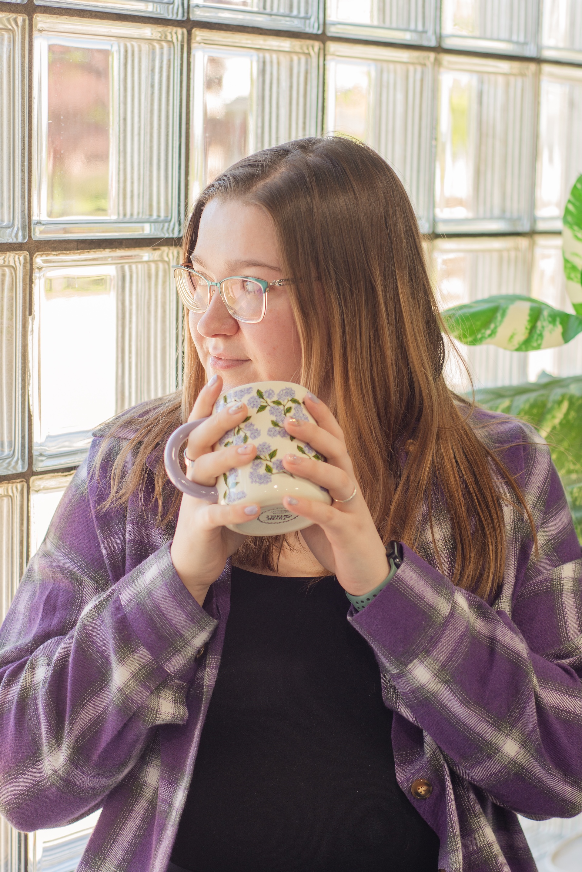 woman in purple drinks coffee in front of a window