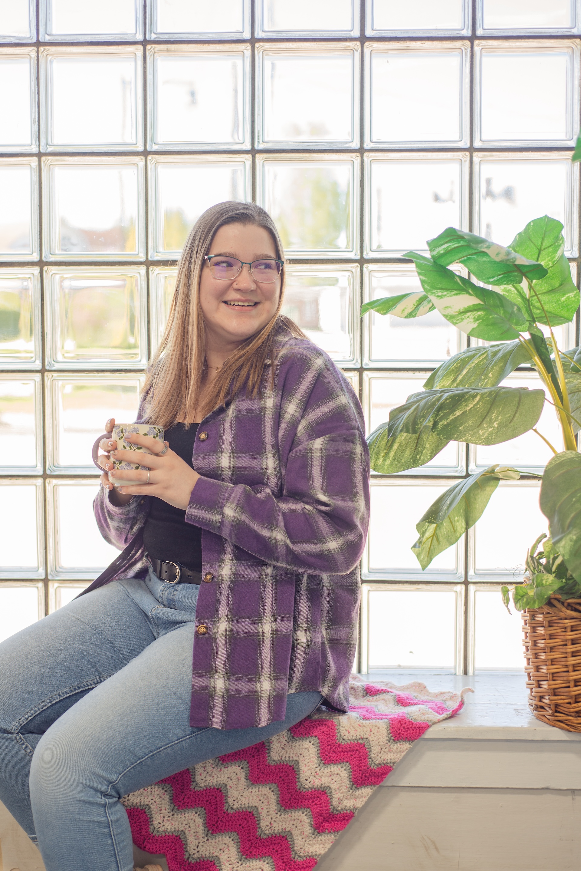 Courtney in purple drinks coffee in front of a window