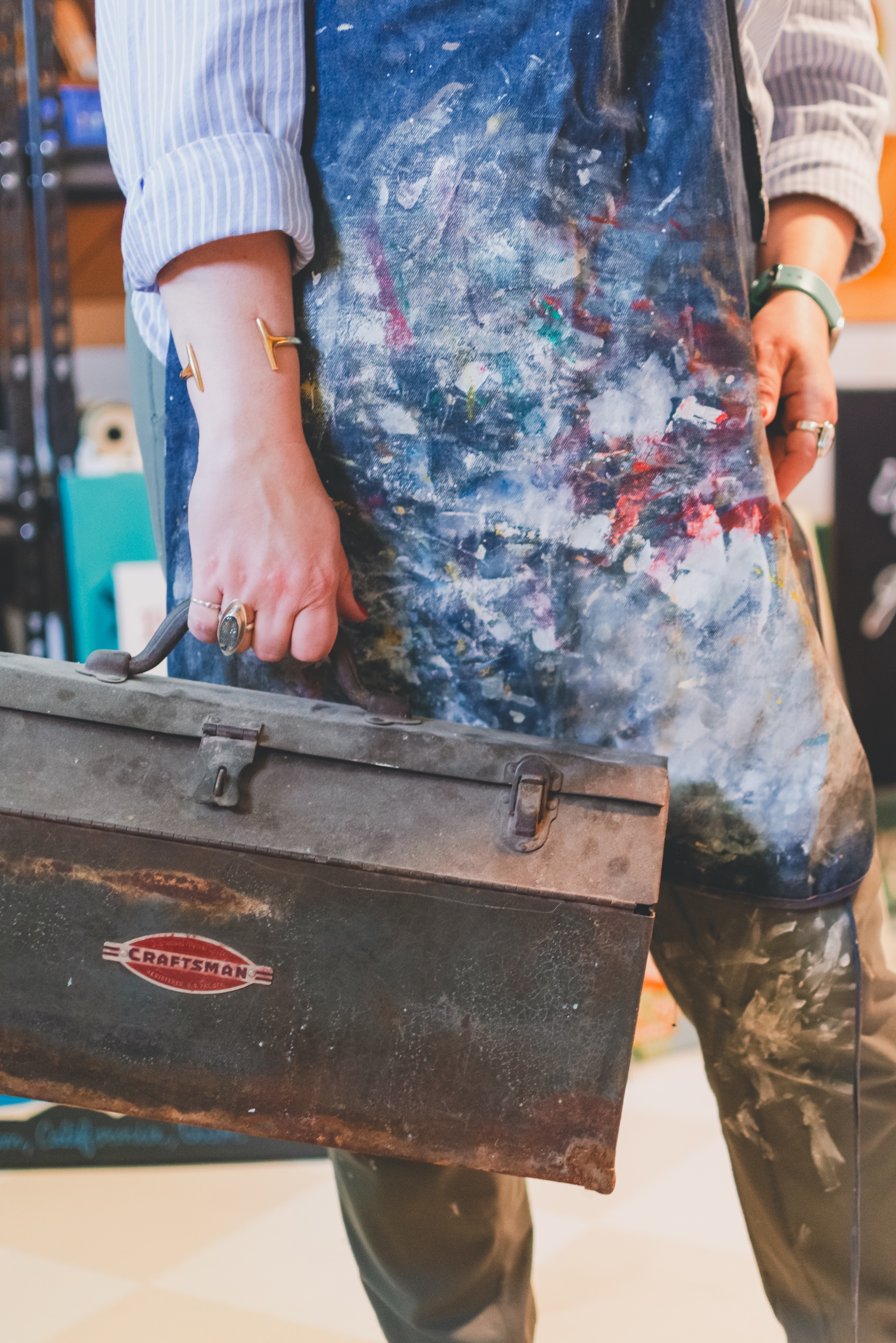 Close up of muralist holding art kit with a paint covered smock during a personal branding session